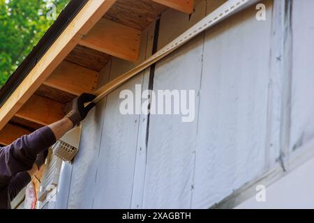 Beim Bau des Hauses nagelt der Handwerker J-Kanal Vinylverkleidungen, bevor er sie für die Verkleidung einbaut Stockfoto