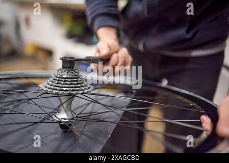 Wartung eines Fahrrads: Nicht erkennbarer Werkstattarbeiter, der den Kettenradsatz eines Radrads in seiner Werkstatt montiert. Echte Menschen bei der Arbeit. Stockfoto