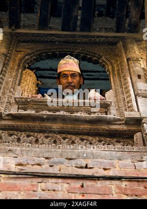 Porträt eines nepalesischen Mannes, der aus dem Fenster seines Hauses in Kathmandu, Nepal, blickt. Stockfoto