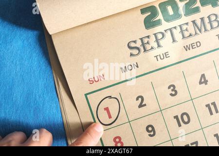 Hand zeigt auf das Datum vom 1. September 2024 auf dem Kalender flach auf blauem Hintergrund. Erinnerung am ersten Tag des Monats. Stockfoto