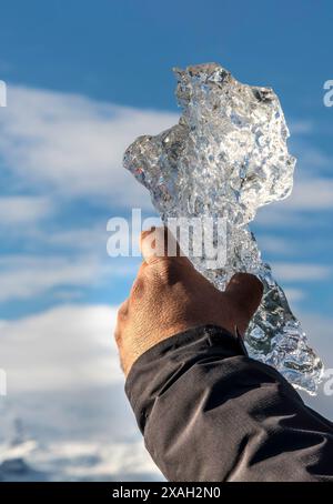 Eine Person hält ein Stück Eis in der Hand. Der Himmel ist blau und im Hintergrund sind Wolken. Die Szene ist ruhig und ruhig, wie die Person h ist Stockfoto