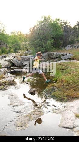 Junge, der im Sommer über einen Bach in der Natur springt Stockfoto