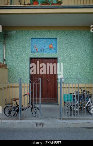 Die Vorderwand eines Hauses am Wasser in Monterosso al Mare, grüne Mosaikfliesen und eine Mosaikplatte über der Vordertür goldene Fische in einem blauen Meer Stockfoto