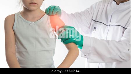 Ein orthopädischer Traumatologe untersucht die Schulter eines kleinen Mädchens mit grünen medizinischen Handschuhen. Hypothermie und Entzündung des Schultergelenks, Stockfoto