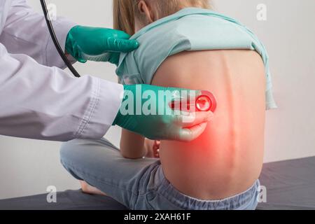 Ein Arzt in grünen medizinischen Handschuhen lauscht den Bronchien mit einem Stethoskop eines siebenjährigen kleinen Mädchens. Das Konzept der Atemwegserkrankung, bron Stockfoto