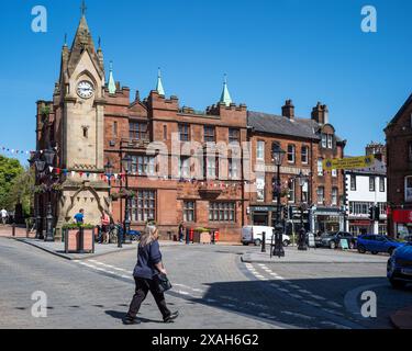 Sie überqueren den Marktplatz mit dem Musgrave Monument, der Barclays Bank und dem Advertiser Office im Hintergrund, Penrith, Westmorland & Furness, Großbritannien Stockfoto