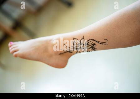 Dieses Bild zeigt eine Nahaufnahme eines weiblichen Fußgelenks mit einem Henna-Tattoo. Das Tattoo ist ein kompliziertes Design einer Blume und Reben. Das Bein der Frau ist hoch, s Stockfoto