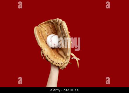 Hand in Leder Baseballhandschuh hält weißen Baseball auf rotem Hintergrund. Hochwertige Fotos. Gewinner Stockfoto