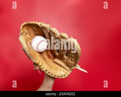 Baseballhandschuh aus Leder mit weißem Baseball auf weiblicher Hand auf rotem Hintergrund. Hochwertiges Foto. Gewinner Stockfoto