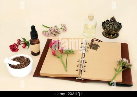 Baldrian Adaptogen Kräuterwurzel mit Blumen, Notizbuch und ätherischen Ölflaschen. In der pflanzlichen Medizin zur Behandlung von Schlaflosigkeit verwendet, ist ein Beruhigungsmittel. Stockfoto