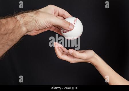 Mann Hand wirft einen Baseball in eine Frauenhand auf schwarzem Hintergrund Stockfoto