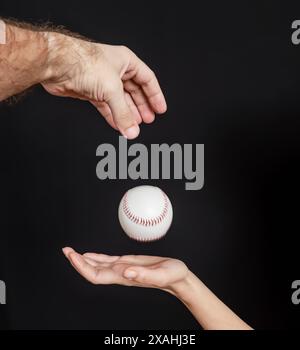 Mann Hand wirft einen Baseball in eine Frauenhand auf schwarzem Hintergrund Stockfoto