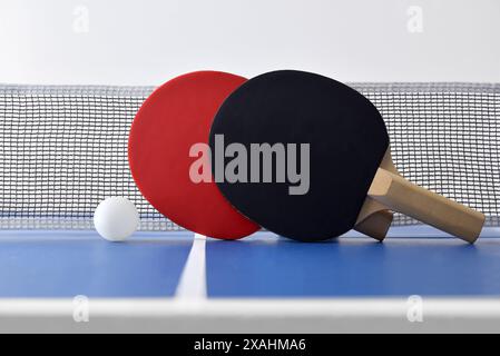 Blick auf Tischtennisset mit Paddles auf dem Netz und blauem Spieltisch mit weißer Kugel. Vorderansicht. Stockfoto