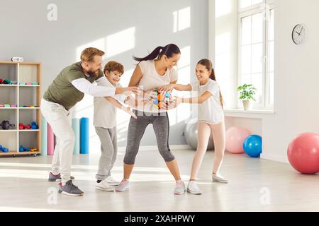 Aktive Familie mit zwei Kindern spielt mit bunten Bällen in der hellen Sporthalle. Stockfoto