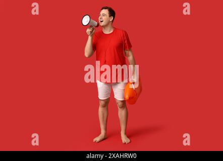 Männlicher Rettungsschwimmer mit Rettungsboje und Megaphon auf rotem Hintergrund Stockfoto