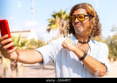 Lächelnder Mann im Strandurlaub, der sich mit einem Freund über Selfie redet. Stockfoto