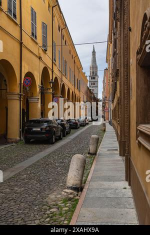 Cesare Battisti Straße in Modena, antike Gebäude mit farbenfrohen Arkaden und dem Domturm im Hintergrund, Italien. Stockfoto