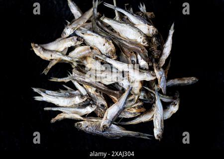 Kleine Fische, getrocknet in Salz. Indonesische Gewürze. Getrockneter Fisch und Sardellen auf schwarzem Hintergrund. Salzige Meeresfrüchte, getrockneter Fisch. Sardellen und Widder, sma Stockfoto