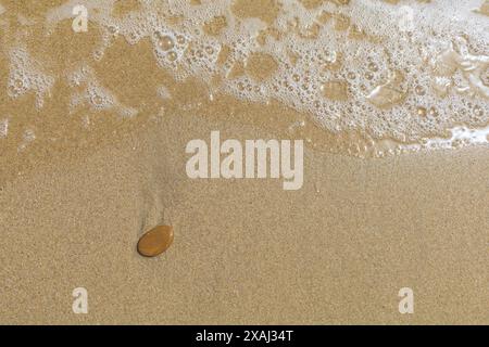 Nahaufnahme eines flachen Fotos eines nassen Sandstrandes mit Gezeiten und kleinem braunen Stein Stockfoto