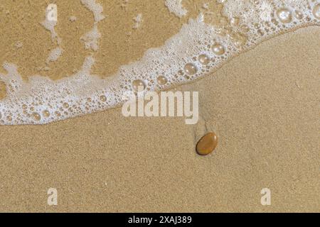 Nahaufnahme eines flachen Fotos eines nassen Sandstrandes mit Gezeiten und kleinem braunen Stein Stockfoto