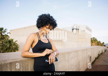 Frau überprüft ihre Smartwatch, bevor sie trainiert. Junge Frau, die sich vor einem Lauftraining vorbereitet und ihren Fitnessfortschritt überwacht. Stockfoto