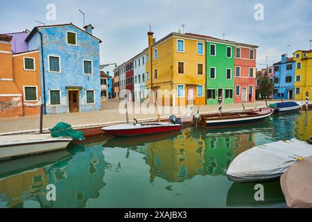 Wunderschöne farbenfrohe Hausfassade auf Burano Island, Norditalien. Halb orange, halb blaue Hauswand mit einer gelben Tür und zwei Fenstern mit Pflanzen Stockfoto