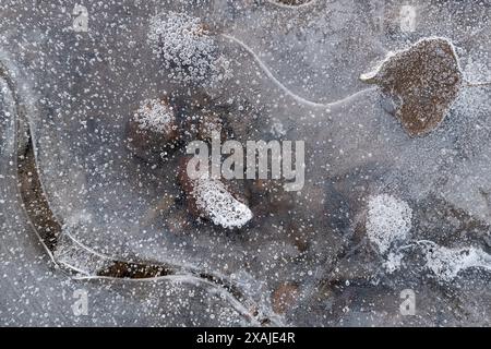 Oberfläche gefrorener Pfütze, Kies mit Blasen und trockenem Blatt in durchscheinendem Eis Stockfoto