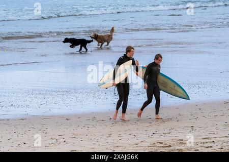 Zwei männliche Surfer, die ihre Surfbretter tragen und am Fistral Beach in Newquay in Cornwall in Großbritannien aus dem Meer gehen. Stockfoto