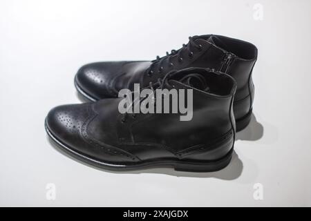 Stilvolle schwarze Stiefel mit Brogue-Design auf einer sauberen weißen Oberfläche, die Eleganz und Raffinesse im Schuhdesign ausstrahlen Stockfoto
