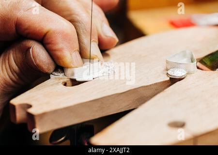 Nahaufnahme der Hand des Juweliers, die mit einer Juweliersäge auf der Bank arbeitet Stockfoto