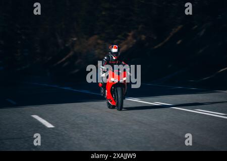 Motorradfahrer lehnen sich zwischen Schatten und Sonnenlicht auf ein rotes Rennrad Stockfoto