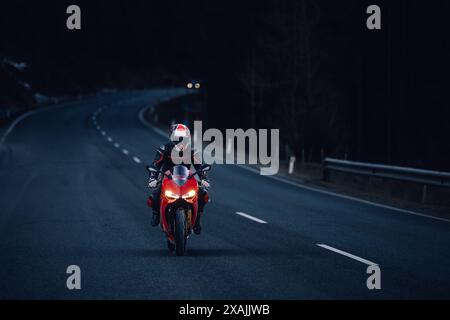 Motorradfahrer lehnen sich im Kurvenschatten und Sonnenlicht auf rotes Rennrad Stockfoto
