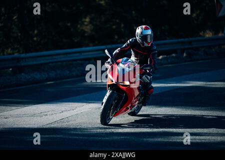 Motorradfahrer lehnen sich im Kurvenschatten und Sonnenlicht auf rotes Rennrad Stockfoto
