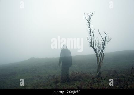 Eine durchsichtige, geisterhafte Figur mit Kapuze. Im Winter auf einem gruseligen, nebligen Moorland stehen. Stockfoto