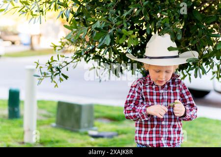 Junger 3-5-jähriger Cowboy unter einem Baum in Cowboyhut und Stiefeln Stockfoto