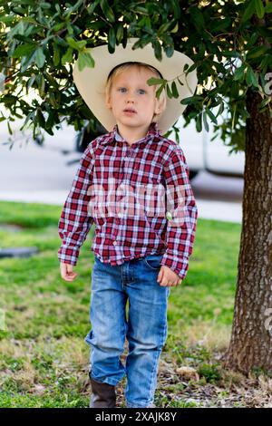 Junger 3-5-jähriger Cowboy unter einem Baum in Cowboyhut und Stiefeln Stockfoto