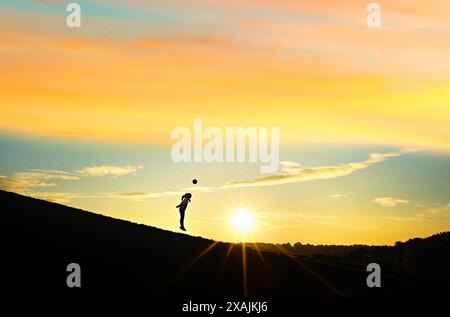 Silhouette, junges Mädchen, das bei Sonnenuntergang Fußball schlägt Stockfoto