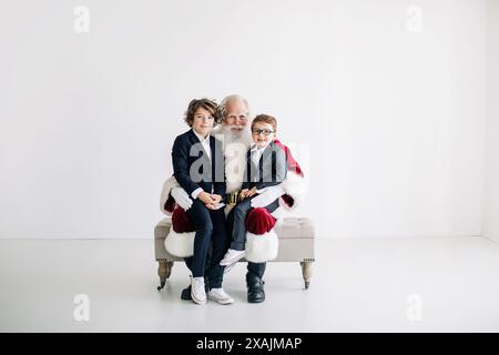 Weihnachtsmann mit zwei Jungs in Anzügen, die auf einer Bank gegen einen Minima sitzen Stockfoto