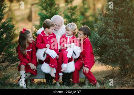 Weihnachtsmann mit vier Kindern im roten Pyjama, die draußen auf einer Bank sitzen Stockfoto