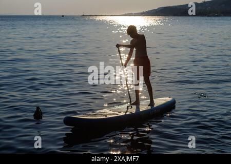 Ein junger Teenager wird von der Sonne beleuchtet, während er auf einem Stand Up Paddle Board auf dem Meer paddelt, Omis, Kroatien. Stockfoto