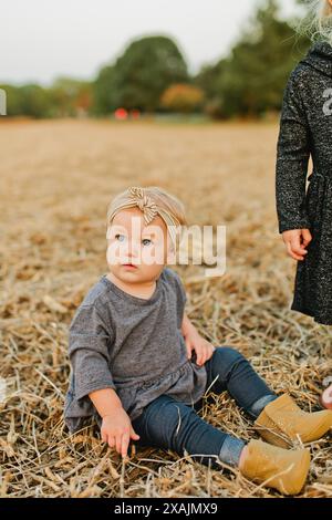 Ein junges Mädchen mit blauen Augen sitzt auf dem Feld mit Schleife auf dem Kopf Stockfoto