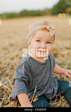 Ein junges Mädchen mit blauen Augen sitzt auf dem Feld mit Schleife auf dem Kopf Stockfoto