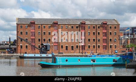 Szene in der historischen Gegend von Gloucester Docks mit Schmalbooten, die vor den Apartments liegen, die in einem typischen Lagerhaus in Großbritannien untergebracht sind Stockfoto