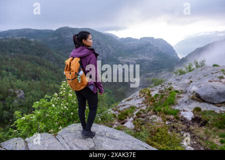 Ein Wanderer steht auf einem felsigen Abgrund mit Blick auf einen atemberaubenden norwegischen Fjord, umgeben von Nebel und Wolken. Preikestolen, Norwegen Stockfoto