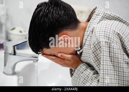 Morgenroutine, Junge im Schlafanzug, der sein Gesicht im Bad wäscht Stockfoto