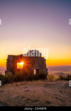 Mauern der Burgruine Desenberg in der Warburger Börde scheint die aufgehende Sonne durch die Öffnung in der Mauer und bildet einen Sonnenstern. Warburg, Landkreis Höxter, Nordrhein-Westfalen, Deutschland Stockfoto