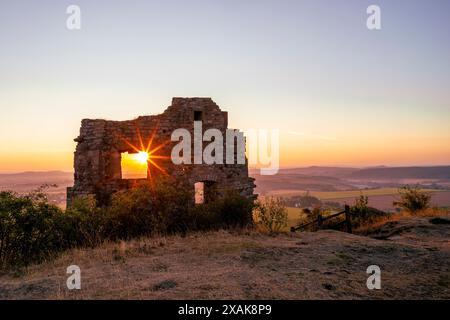 Mauern der Burgruine Desenberg in der Warburger Börde scheint die aufgehende Sonne durch die Öffnung in der Mauer und bildet einen Sonnenstern. Warburg, Landkreis Höxter, Nordrhein-Westfalen, Deutschland Stockfoto