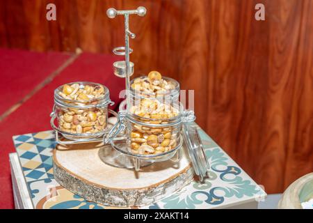 Frittierter Mais und getrocknete und gesalzene Früchte in Glasgläsern in einem alten und gebrauchten Metallkörper. Selektiver Fokus auf das vordere Gefäß. Stockfoto