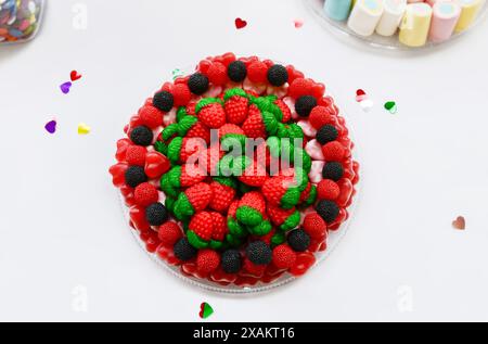 Blick von oben auf leckere Gelee-Süßigkeiten in Form von roten Erdbeeren und schwarzen und roten Brombeeren auf einem Teller auf weißem Hintergrund. Stockfoto