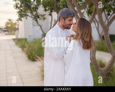 Reisen Sie in die Vereinigten Arabischen Emirate, Abu Dhabi. Arabisches Paar besucht den Park in der Nähe der Großen Moschee in Abu Dhabi in traditioneller Kleidung. Stockfoto